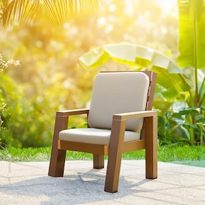 May include: A wooden outdoor chair with a light beige cushion and backrest. The chair has a brown frame and armrests. The background features lush green foliage and sunlight, suggesting a patio or garden setting.