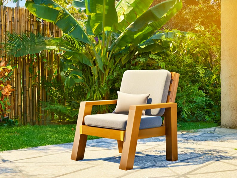 May include: A wooden outdoor armchair with a light gray cushion and a small lumbar pillow. The chair has a natural wood finish and is set on a stone patio with lush greenery in the background. The chair is designed for outdoor use.