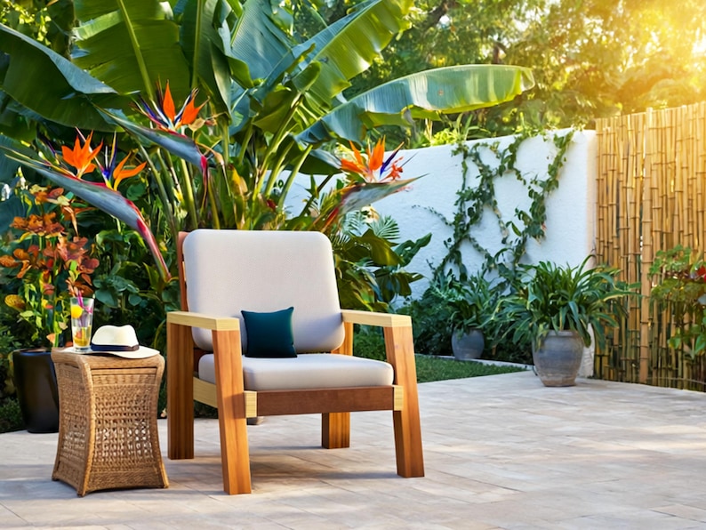 May include: Outdoor patio scene featuring a wooden armchair with a cream-colored cushion and a small, dark blue pillow. A woven side table holds a hat and a drink. Lush greenery and bird of paradise flowers surround the seating area.