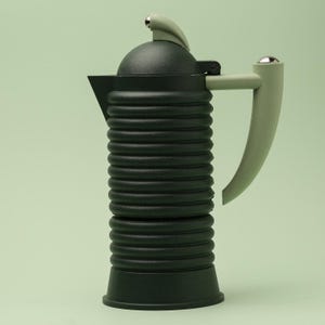 Puede incluir: Una cafetera negra y verde claro con un cuerpo acanalado y un asa curva. La cafetera tiene una parte superior redondeada con una pequeña palanca curva y un acento plateado. El asa y la palanca son de color verde claro.