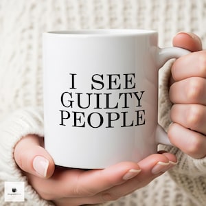 May include: White ceramic mug with the text "I SEE GUILTY PEOPLE" in black, held by a person. The mug has a standard handle and a glossy finish. The background is a soft, neutral color.