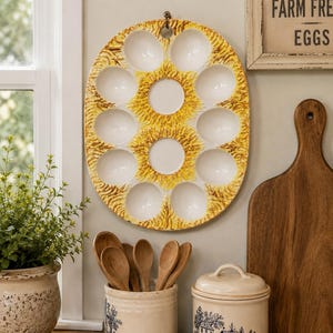 May include: Oval ceramic egg holder with a yellow and brown design, holding 12 eggs. The kitchen scene includes a wooden cutting board, a ceramic jar with wooden spoons, and a matching jar with a lid. A sign reads "Farm Fresh Eggs."