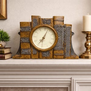 May include: A decorative mantel clock with a round face and Roman numerals, set within a faux-book design. The clock is flanked by a candle holder and a small potted plant, creating a classic home decor scene.