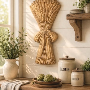 May include: A wall-mounted decorative wheat sheaf sculpture in a tan, textured finish, featuring a central tied bow design. The piece is vertically oriented and displays detailed stalks of grain fanned out at the top and bundled at the base.