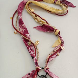 Può includere: Un cordino per telefono fatto a mano con tessuto paisley bordeaux e giallo. Il cordino è decorato con piccoli ciondoli dorati e conchiglie. Include un moschettone nero e un cordino bordeaux.