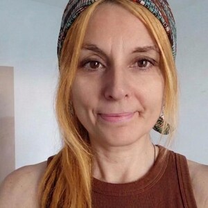 Könnte beinhalten: Eine Frau mit langem, hellem Haar und einem gemusterten Stirnband. Sie trägt ein braunes Tanktop. Das Stirnband hat eine Mischung aus Farben, darunter Braun, Türkis und Rot. Der Hintergrund ist hellblau.
