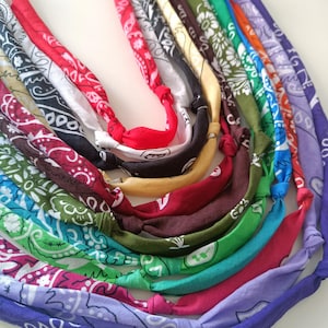 Puede incluir: Una colección de pañuelos coloridos, anudados para formar un collar. Los pañuelos muestran varios patrones, incluyendo diseños de cachemira y florales, en tonos de rojo, azul, verde y morado. La imagen es un primer plano.