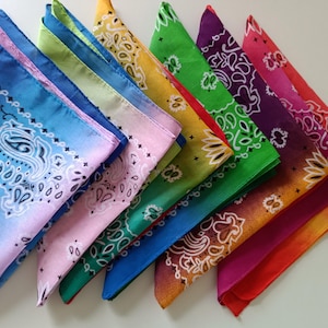 May include: A selection of bandanas in various colours, each with a paisley pattern. The bandanas are arranged in a row, with colours including blue, pink, green, yellow, purple, and red. They are folded into triangles.