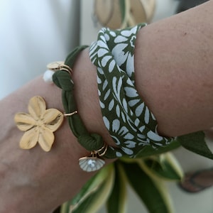 Può includere: Sono mostrati due braccialetti. Uno è verde oliva con un ciondolo a forma di fiore dorato e altri ciondoli dorati. L'altro è un motivo floreale verde e bianco. I braccialetti sono indossati al polso.