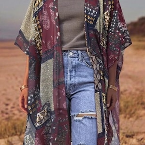 Puede incluir: Un kimono transparente de frente abierto con un diseño de patchwork de patrones de cachemira y geométricos en tonos burdeos, azul marino y crema. La prenda se lleva sobre una camiseta de tirantes gris y vaqueros azul claro desgastados.