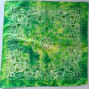 May include: A square, green bandana with a paisley design. The bandana features a vibrant green and yellow tie-dye pattern, with white and black paisley and floral motifs. The bottom right corner reads "100% Cotton".