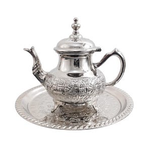 Peut inclure: Une théière argentée avec des motifs en relief complexes, un bec verseur incurvé et un couvercle décoratif. La théière est posée sur un plateau rond assorti avec un bord perlé. L'ensemble est conçu pour servir le thé.