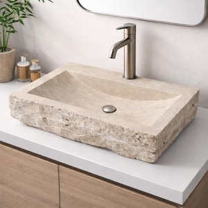 Op de afbeelding: Een rechthoekige, beige stenen badkamer wastafel met een kraan van geborsteld nikkel. De wastafel heeft een natuurlijke, gebeitelde rand en een gebogen binnenbekken. Een kleine, ronde afdekking is zichtbaar.