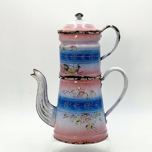 Könnte beinhalten: Eine antike Kaffeekanne aus Emaille mit einem rosa-blauen Blumendesign. Die Kanne hat ein zweistufiges Design mit einem abnehmbaren Deckel zum Brühen von Kaffee.