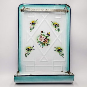 Peut inclure: Un porte-ustensiles en émail vintage avec un motif floral bleu et blanc. Le porte-ustensiles a une barre en métal pour suspendre des objets et une étagère en dessous. Le porte-ustensiles est parfait pour ranger les ustensiles de cuisine ou d'autres petits objets.