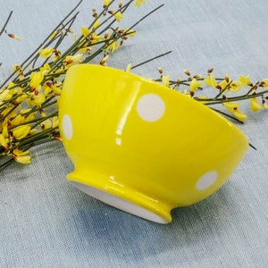 May include: A yellow ceramic bowl with white polka dots. The bowl is on a light blue fabric background.