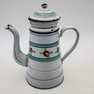 Könnte beinhalten: Weiße Emaille-Kaffeekanne mit Blumenmuster und blauem Rand. Die Kanne hat einen Deckel mit einem kleinen Ausguss.
