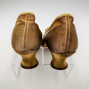 May include: A pair of gold satin heeled shoes with a pointed toe. The shoes are on a white background.