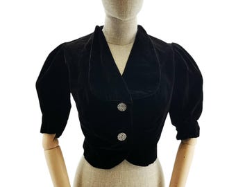 May include: A black velvet cropped jacket with a wide collar and puffed sleeves. The jacket has two decorative buttons with rhinestones.