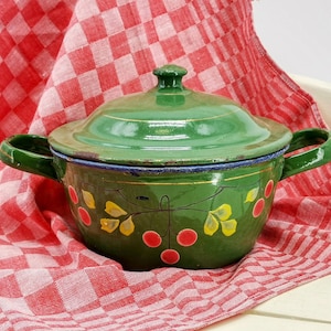 Puede incluir: Una olla de esmalte verde con tapa y dos asas. La olla está decorada con un diseño floral con hojas amarillas y cerezas rojas.