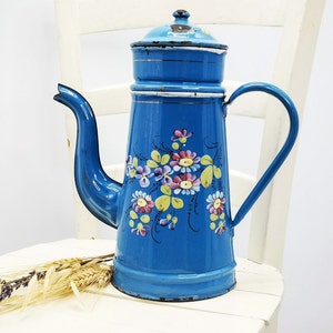 Könnte beinhalten: Eine blaue Emaille-Kaffeekanne mit Blumenmuster. Die Kanne hat einen weißen Rand und einen weißen Griff.