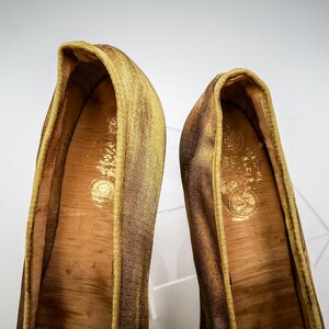May include: A pair of gold satin slippers with a brown leather insole. The slippers have a pointed toe and a low heel.
