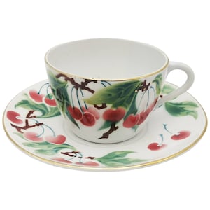 Puede incluir: Una taza de té y un platillo blancos con un borde dorado. La taza y el platillo están decorados con un diseño de flor de cerezo en tonos de verde, rojo y blanco.