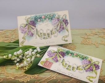 May include: Two vintage postcards with a floral design featuring purple and green flowers. The text on the cards reads "Bonne Année" which is French for "Happy New Year".