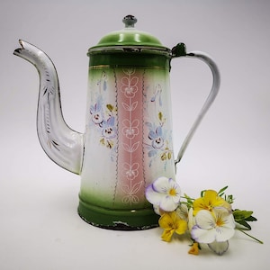 May include: A vintage green, white, and pink enamel coffee pot with floral designs. The pot has a spout and a handle. A bouquet of white and yellow pansies are in front of the pot.