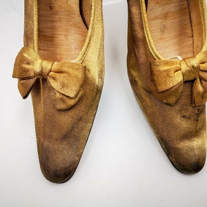May include: A pair of gold satin shoes with a bow on the toe.