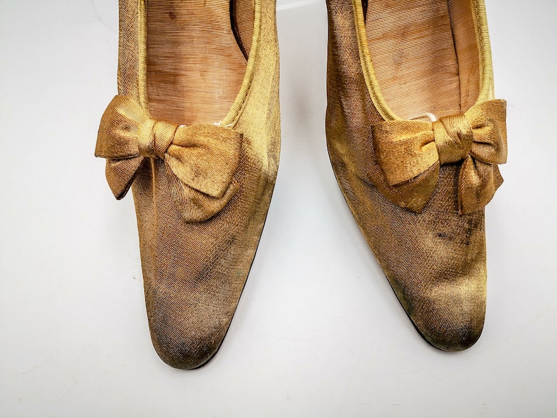 May include: A pair of gold satin shoes with a bow on the toe.