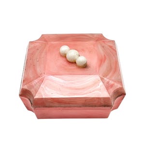 Op de afbeelding: Een vierkante, roze decoratieve doos met een marmer effect en drie witte bollen binnenin. De doos heeft een geometrisch ontwerp met gebogen randen en een glanzende afwerking, ideaal voor het opbergen van kleine items.