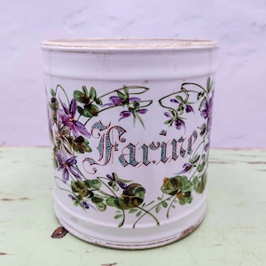 May include: White ceramic jar with a floral design featuring purple flowers and green leaves. The jar has the word "Farine" written in cursive on the front.
