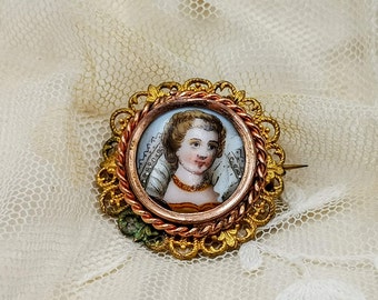 Peut inclure: Une broche dorée et cuivrée avec un motif de filigrane délicat. La broche présente un camée rond avec un portrait peint d'une femme portant un voile blanc.
