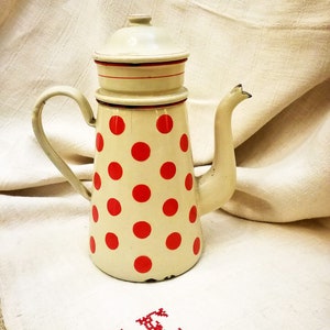 Puede incluir: Cafetera de esmalte blanco con lunares rojos y una banda roja alrededor de la tapa. La cafetera tiene un pico y un asa.