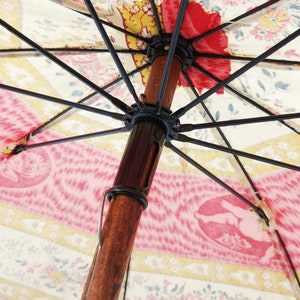 Antique French child's parasol in cretonne fabric with a design of floral garlands and cherubs in oval medallions, in tones of coral, pink, beige, honey and sage green, wooden handle with hand painted face.
