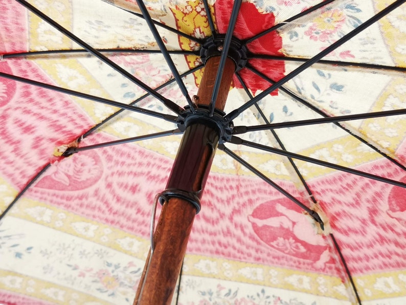 Antique French child's parasol in cretonne fabric with a design of floral garlands and cherubs in oval medallions, in tones of coral, pink, beige, honey and sage green, wooden handle with hand painted face.