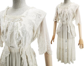 Puede incluir: Un vestido blanco de algodón con detalles de encaje y bordados. El vestido tiene un escote con volantes y un corpiño ajustado. La falda es amplia y fluida, con capas de encaje y volantes.