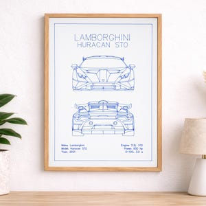 Op de afbeelding: Een ingelijste print in blauwdrukstijl van een Lamborghini Huracan STO. De print toont voor- en achteraanzichten van de auto in blauwe lijnen tegen een witte achtergrond. De lijst is van lichtgekleurd hout.