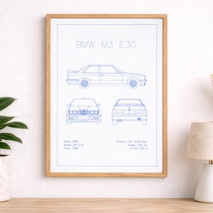 Peut inclure: Impression encadrée d'un plan de BMW M3 E30 en lignes bleues sur fond blanc. Le dessin présente la voiture de côté, de face et de dos, avec des détails techniques. Le cadre est de couleur marron clair. Mesures en cm.