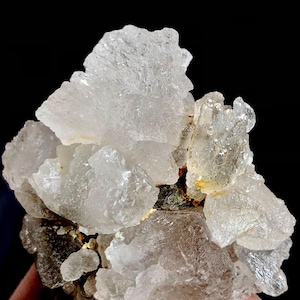 Puede incluir: Un grupo de formaciones minerales cristalinas translúcidas. Los cristales tienen una superficie rugosa y texturizada, con tamaños variables y una mezcla de áreas claras y opacas. El fondo es negro, resaltando los detalles del mineral.