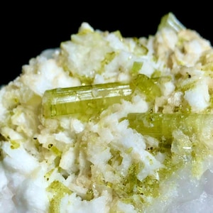 Peut inclure: Gros plan d'un spécimen minéral présentant des formations cristallines blanches avec des cristaux vert-citron translucides et vibrants. Le minéral a une surface rugueuse et texturée sur fond sombre.