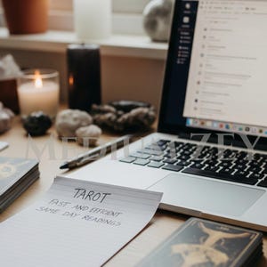 May include: A laptop, tarot cards, candles, and crystals are arranged on a wooden surface. A notepad reads "Tarot, Fast and Efficient, Same Day Readings." The laptop screen displays a website or application.