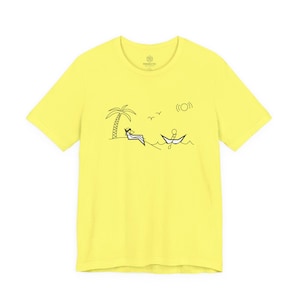May include: A yellow t-shirt featuring a black and white illustration of a beach scene. The design includes a palm tree, a person relaxing on a beach chair, a person in a boat, the sun, and birds. The shirt has a crew neck and short sleeves.