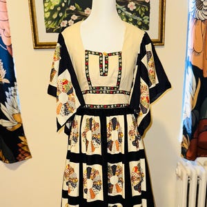 May include: A vintage dress displayed on a mannequin. The dress has a cream-coloured bodice with a square neckline and decorative trim. The sleeves and skirt are black with colourful, circular patchwork designs. The dress has a defined waist and a flowing skirt.