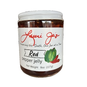 Puede incluir: Un tarro de mermelada de pimiento rojo con tapa y etiqueta blancas. La etiqueta presenta el texto "Lauri Jo's" en escritura roja, junto con "Red pepper jelly" y un gráfico de pimientos verdes y chiles rojos. Peso neto 227g.