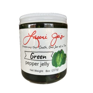 Puede incluir: Un tarro de gelatina de pimiento verde con tapa blanca y etiqueta que dice "Lauri Jo's". La etiqueta también dice "Preserving the South, One Jar at a Time" y "Green pepper jelly". Peso neto 227g.