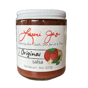 Puede incluir: Un tarro de cristal de salsa Original Lauri Jo's con tapa blanca. La etiqueta presenta una ilustración de tomate rojo, ajo y pimiento verde. El tarro contiene 227g de salsa y el texto "Preserving the South, One Jar at a Time."