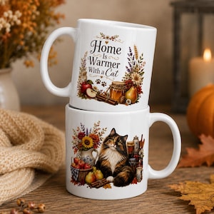 Puede incluir: Dos tazas de cerámica blanca apiladas verticalmente. La taza superior presenta el texto "Home Is Warmer With a Cat" rodeado de ilustraciones de flores, un tarro de miel, ramas de canela y una pera. La taza inferior muestra un gato tricolor.