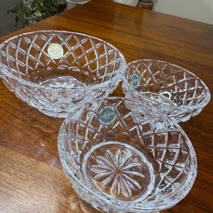 May include: Three clear crystal bowls featuring a diamond-cut pattern on the exterior and a starburst design on the base. Each bowl has a circular sticker with the text Lenox Fine Crystal Made in Czech Republic attached to the glass surface.